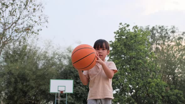 Cheerful cute girl playing basketball outdoors. alt
