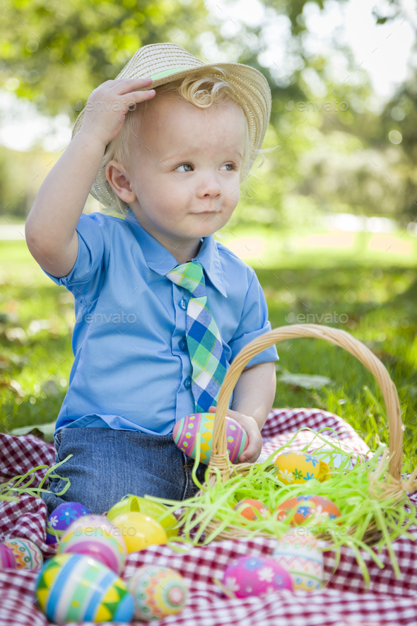 Cute Little Boy Outside On Picnic Blanket Holding Easter Eggs Tips His Hat.