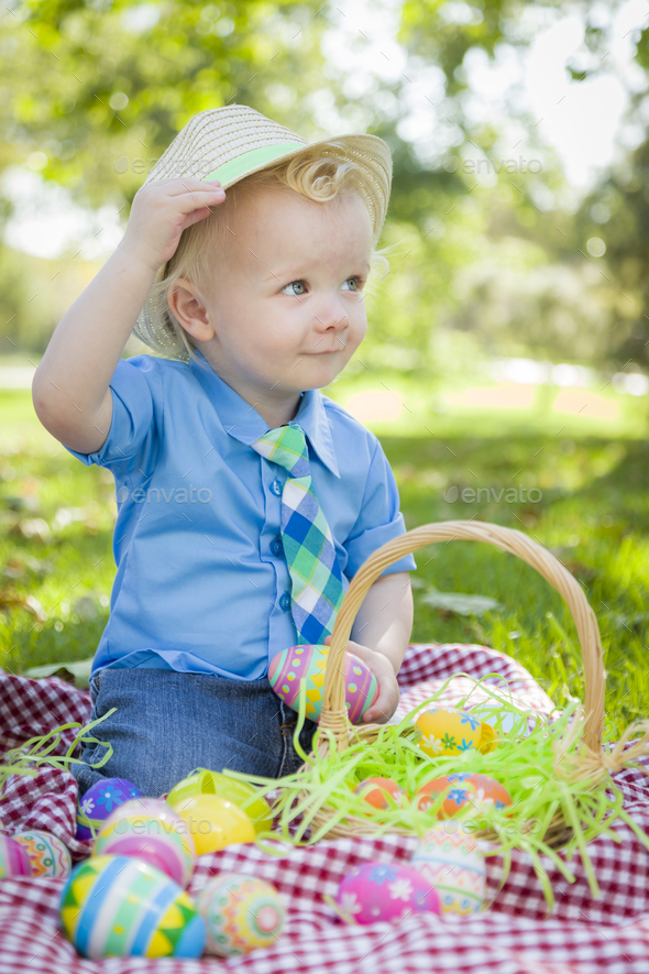 Cute Little Boy Outside On Picnic Blanket Holding Easter Eggs Tips His Hat.