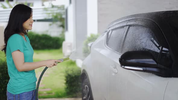 slow-motion of young woman water spray her car with water tube washing it