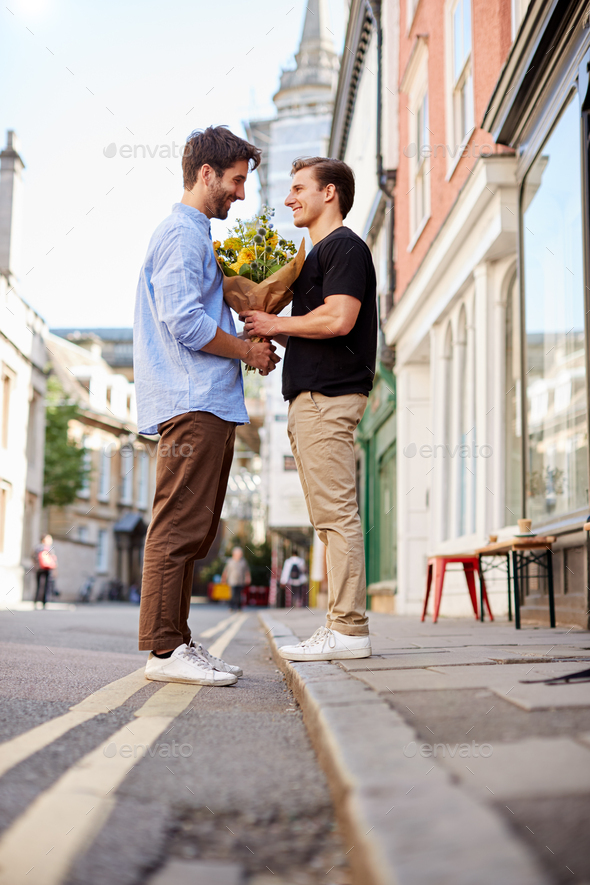 Loving Male Gay Couple On Date Exchanging Bunch Of Flowers In Street