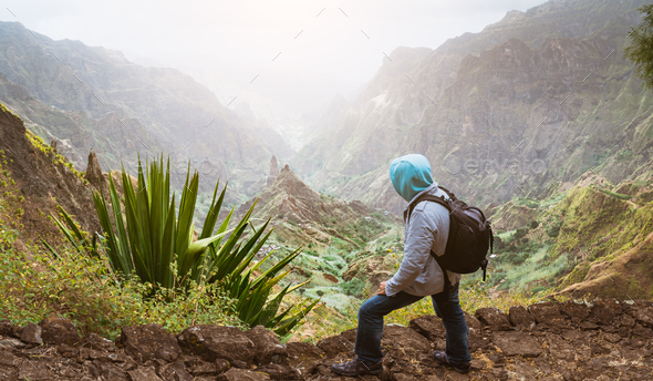 Traveler with backpack looking over the rural landscape with mountain peaks and ravine in dust air