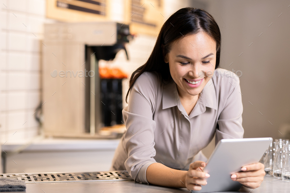 Happy young owner of luxurious restaurant using digital tablet at workplace