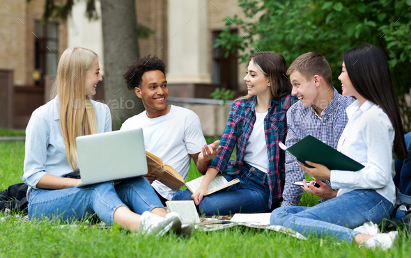 Excited students resting in campus, sitting on grass - Stock Photo - Images