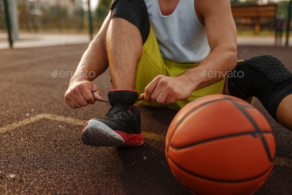 Basketball player tying laces on outdoor court - Stock Photo - Images