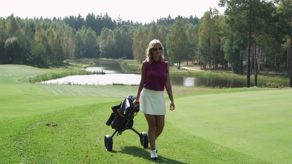 Summer Day Woman Playing Golf Walking with a Cart in Her Hands Golf Clubs in Her Bag View of Golf alt
