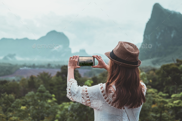 Young woman traveler looking and taking a photo with smartphone at beautiful view - Stock Photo - Images