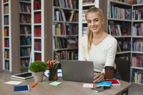 Pretty blonde girl studying with laptop at library - Stock Photo - Images