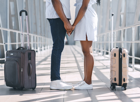 Black millennial couple holding hands at airport, standing with luggage - Stock Photo - Images