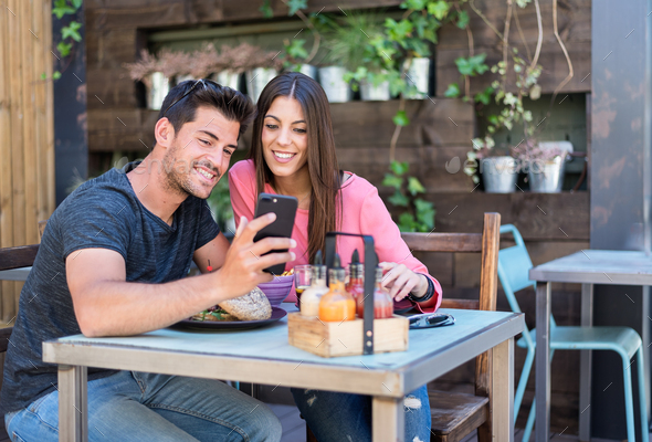 Happy young couple seating in a restaurant terrace with a smartp