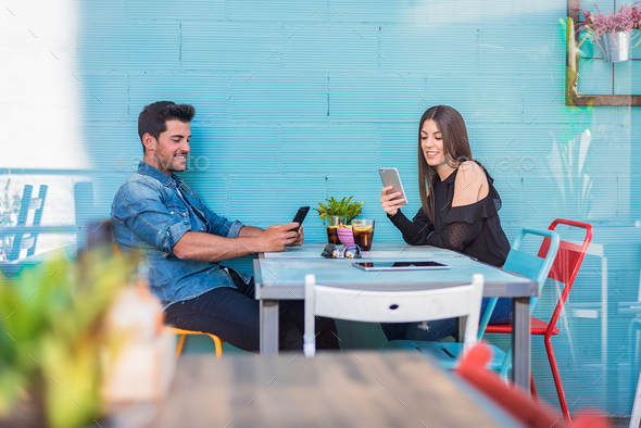 Happy young couple seating in a restaurant with a smartphone
