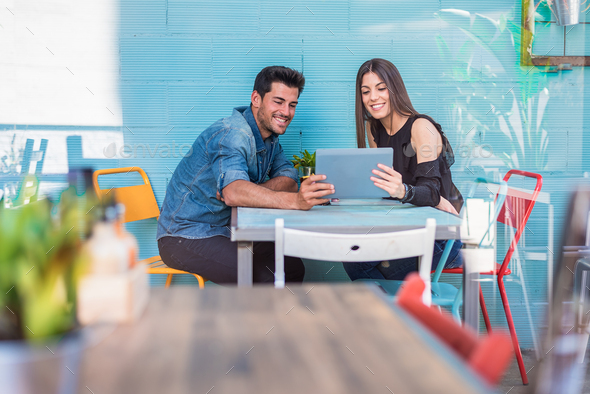 Happy young couple seating in a restaurant with a tablet
