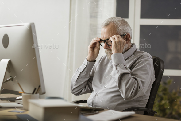 Senior man adjusting his glasses and working with his computer - Stock Photo - Images