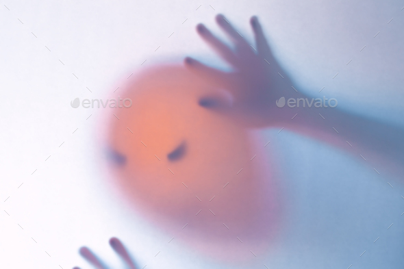 Halloween blurred background. A ghost resembling a pumpkin in color behind glass - Stock Photo - Images