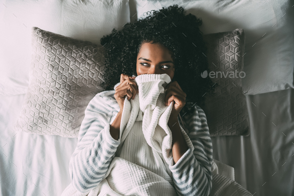 Pretty black woman covering her mouth with the sheet looking away