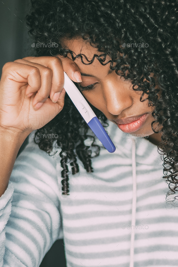 thoughtful worried and sad black woman with pregnancy test in bed