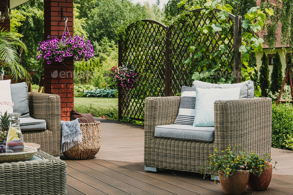 Comfy wicker armchair with pillows on wooden terrace of trendy suburban home
