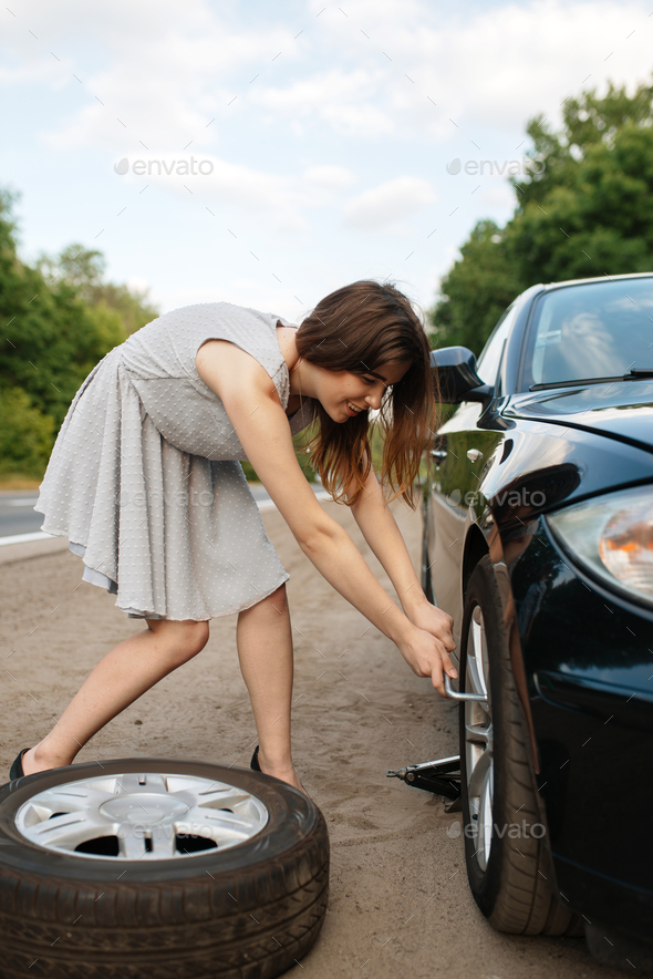 Car breakdown, young woman puts the spare tyre - Stock Photo - Images