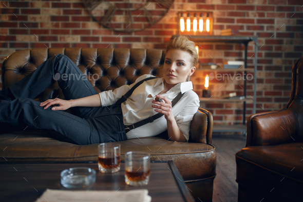 Woman lying on leather couch and smoking cigar