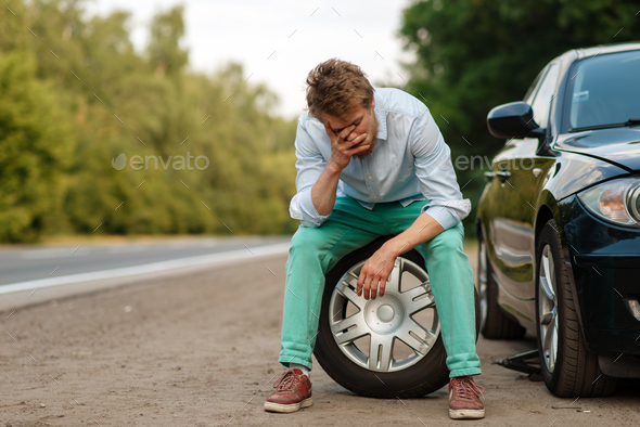 Car breakdown, tired man sitting on spare tyre - Stock Photo - Images
