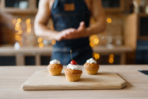 Naked man in apron cooking cakes with cherry - Stock Photo - Images