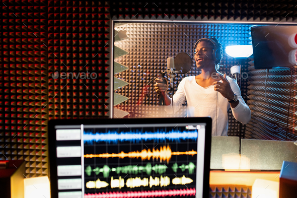 Young man of African ethnicity singing in microphone in sound recording studio
