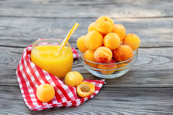 Apricot juice in glass cup with straw and apricots in bowl on wooden table - Stock Photo - Images