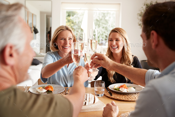 Family With Senior Parents And Adult Offspring Make A Toast Before Eating Meal Around Table At Home