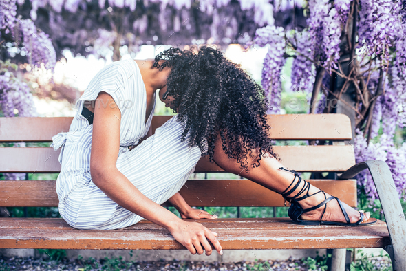 Young sad black woman sitting surrounded by flowers