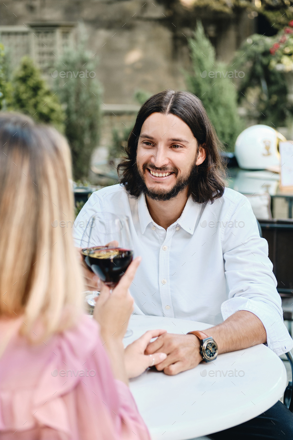 Attractive latin man with glass of wine joyfully looking at girlfriend on romantic date in cafe - Stock Photo - Images