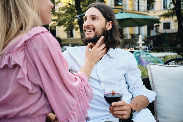 Latin man in shirt with glass of wine happily looking at girlfriend on romantic date in restaurant - Stock Photo - Images