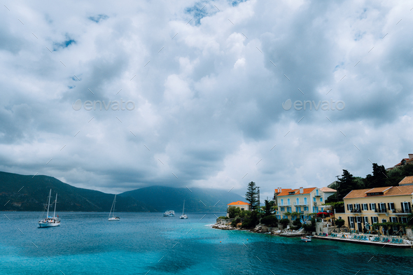 Cloudscape over Fiskardo village buildings with orange brick roofs. Yacht boats looking for shelter - Stock Photo - Images
