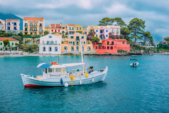 Fishing boat at anchor in blue sea bay of Assos village. Vivid colored houses with clouds in - Stock Photo - Images