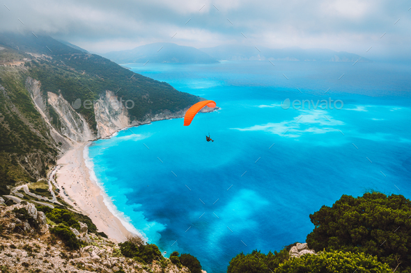 Aerial view of the paraglider flying over gorgeous Myrtos beach. Amazing water colors and beautiful - Stock Photo - Images