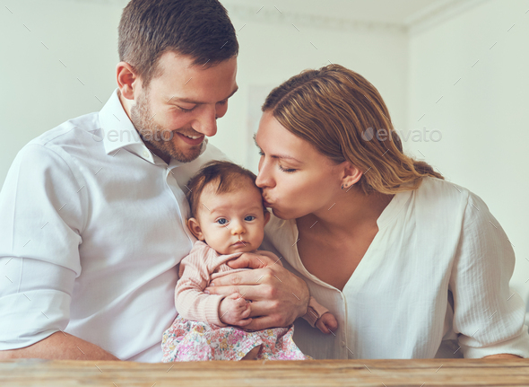 Mother Kissing Her Baby Girl Cradled In Her Husband S Arms Stock Photo By Flamingoimages