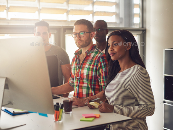 Four diverse workers standing next to computer - Stock Photo - Images