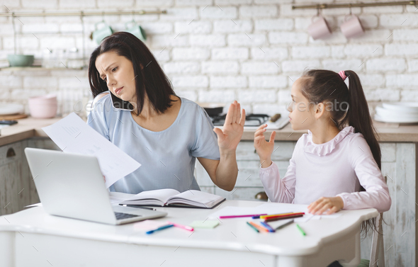 Busy mother frowning and turning away from daughter while working