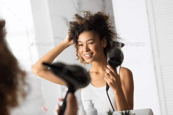 African American Woman Drying Hair With Fan In Bathroom Stock