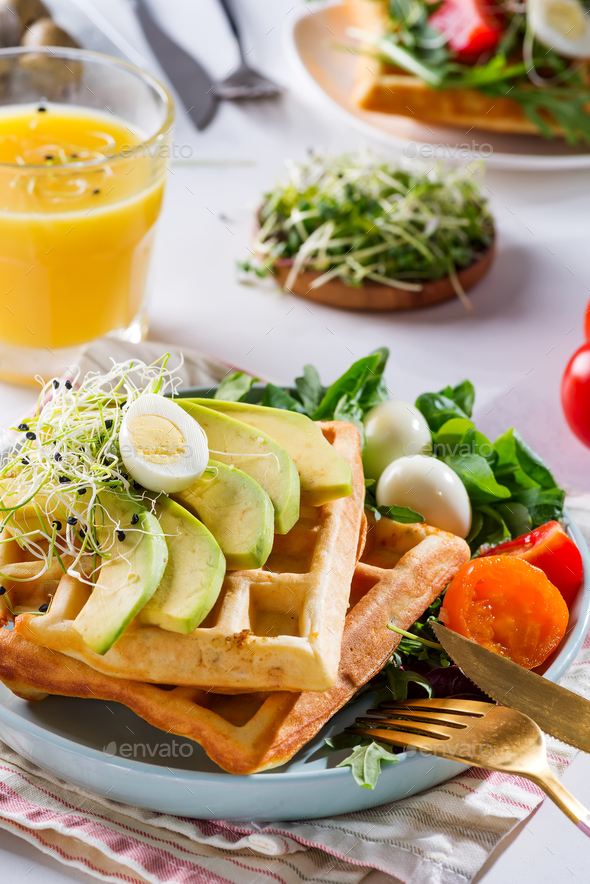 Belgian Waffles with avocado, eggs, micro green and tomatoes with orange juice on marble table - Stock Photo - Images