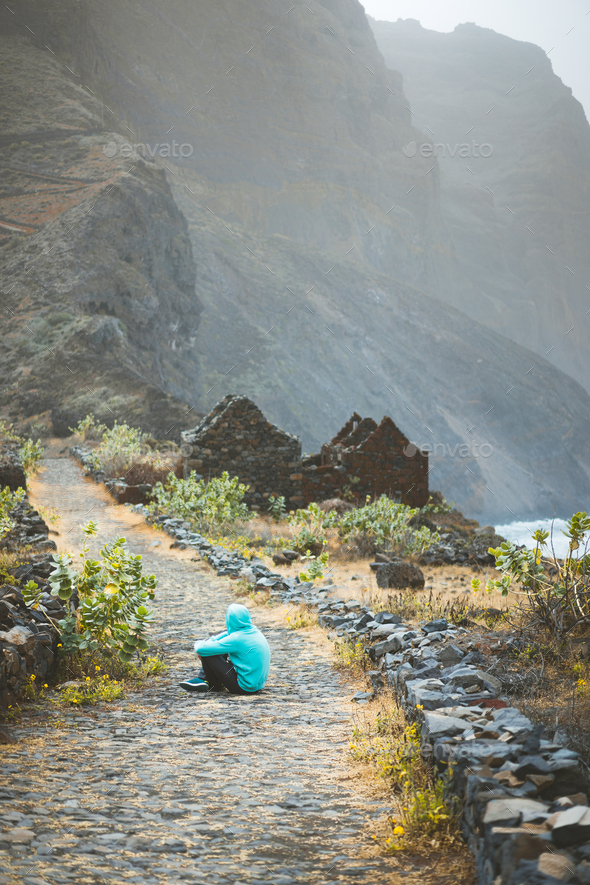 Traveler in hoodie sitting in Aranhas valley in front of amazing rocks with old path from Cruzinha - Stock Photo - Images