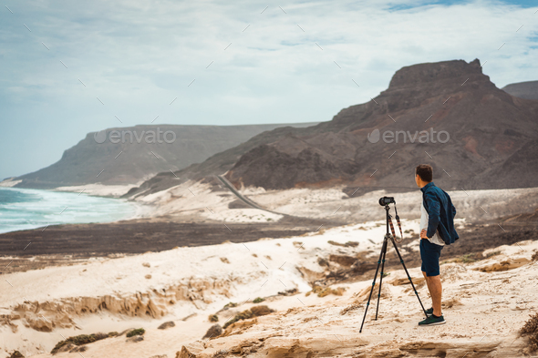 Photographer with camera in desert admitting unique landscape of sand dunes volcanic cliffs on the