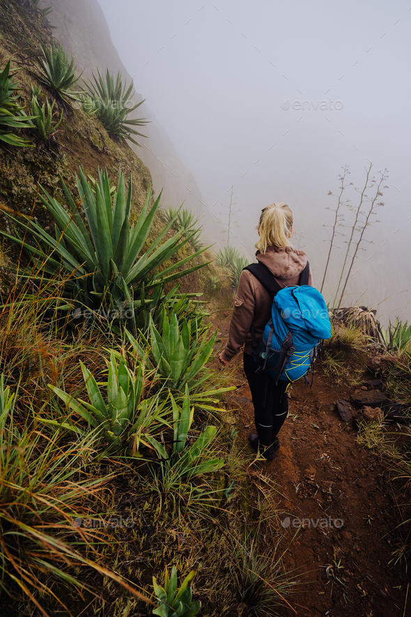 Female traveler staying on the edhe of inactive cove volcano crater above the foggy green valley - Stock Photo - Images