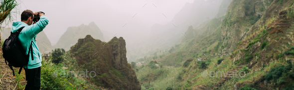 Traveler holding up the camera to take a photo of amazing steep mountainous terrain with lush canyon - Stock Photo - Images