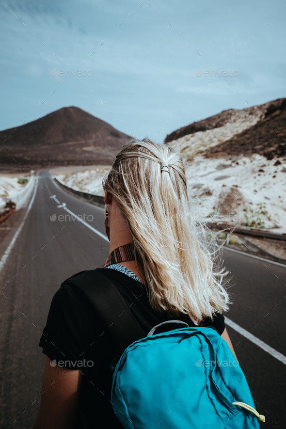 Woman traveler goes on desolate straight road over a surreal landscape with majestic volcano in the - Stock Photo - Images