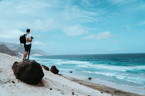 Traveler with camera staying on the black volcanic boulder and admiring unusual barren landscape of - Stock Photo - Images
