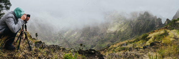 Panoramic shot of traveler making photo of amazing steep mountainous terrain with lush canyon valley - Stock Photo - Images
