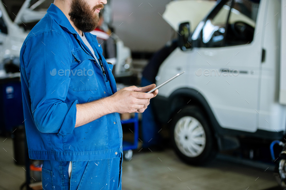 Young contemporary worker in blue uniform surfing for online orders in workshop - Stock Photo - Images