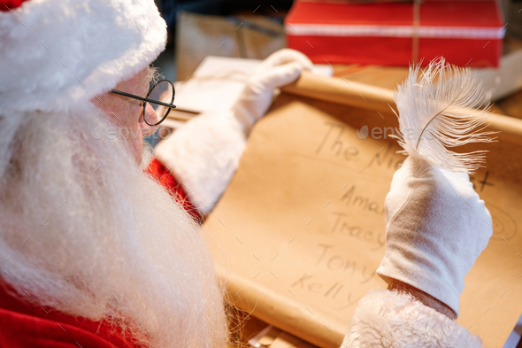 Gloved Santa Claus with feather in hand looking through nice list