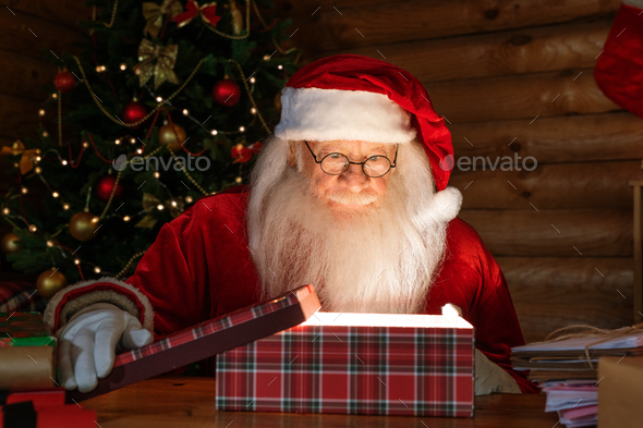 Happy Santa in costume and eyeglasses opening giftbox with magic light inside