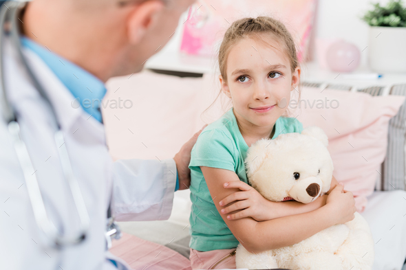 Cute little girl looking at her doctor with smile while listening to him